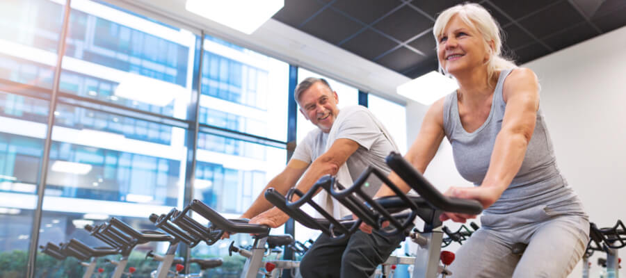An older man and woman exercising indoors on a cycle machine