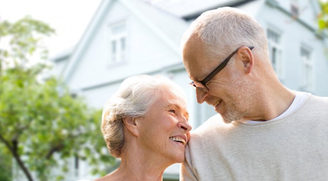 Couple de personnes âgées canadiennes debout devant leur maison et songeant à prendre un prêt sur valeur domiciliaire.